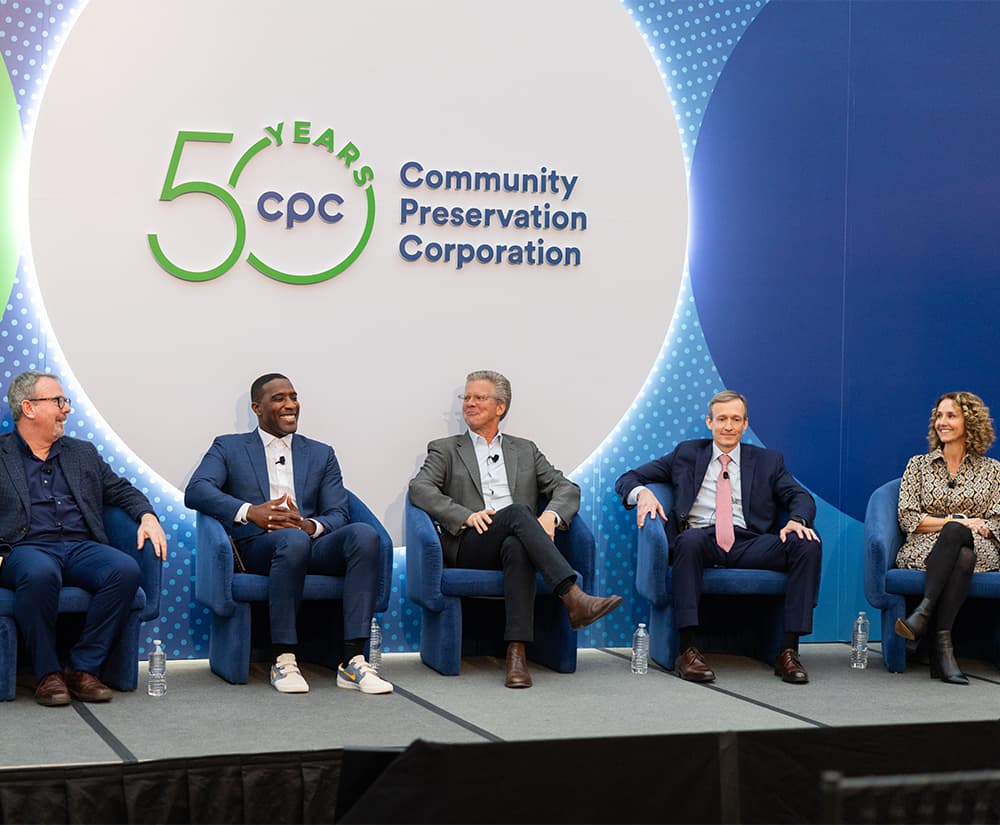 Five seated speakers on stage smiling, looking amused.