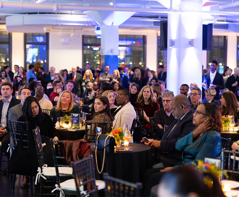 Attendees seated at small tables listening intently.